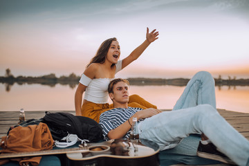 Happy young couple having a date by the river and girl waving to someone