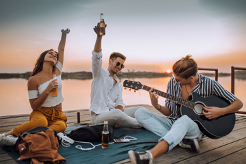 Happy friends playing the guitar and having fun on the beach in the sunset.