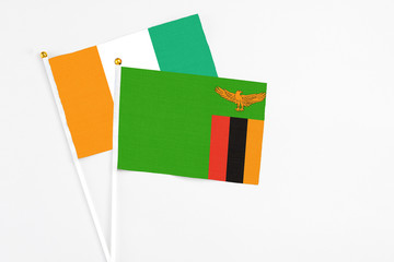 Fototapeta premium Zambia and Cote D'Ivoire stick flags on white background. High quality fabric, miniature national flag. Peaceful global concept.White floor for copy space.