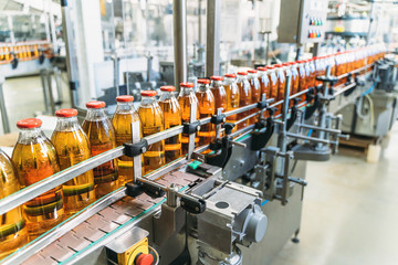 Conveyor belt, juice in bottles on beverage plant or factory interior, industrial production line, selective focus