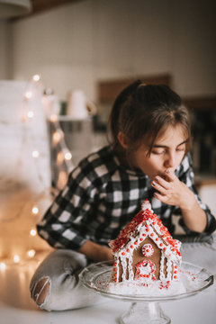 Young girl eating gingerbread house at home. Christmas time