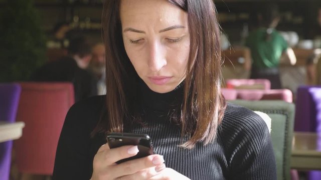 Young wonam use mobile phone while sitting in comfortable coffee shop during work break, charming happy female reading fashion news on cell telephone during breakfast in restaurant.