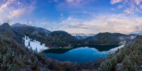 Fototapeta na wymiar lake Alatsee between snowy mountains with forest and nice cloudy sky