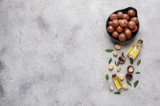 Tasty macadamia nuts with oil on grey background