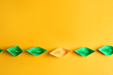 Orange origami boat among green ones on color background. Concept of uniqueness