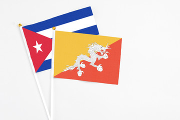 Bhutan and Cuba stick flags on white background. High quality fabric, miniature national flag. Peaceful global concept.White floor for copy space.