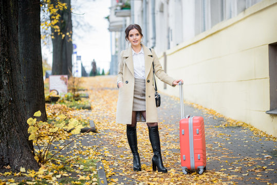 Traveler woman with suitcase in street . Girl tourist goes on Weekend vacation. Photo on the street in the metropolis. autumn yellow leaves, warm cozy autumn
