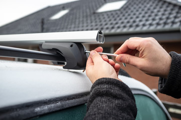 Man with a screwdriver installs attachments for trunk or cargo box on roof of the car.