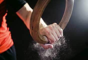 Sport. Muscle-up exercise young man workout at the gym on gymnastic rings with magnesia on the hands.