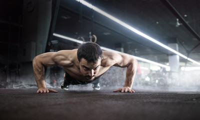Sport. Handsome man doing push ups exercise with one hand in fitness gym.
