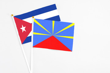 Reunion and Cuba stick flags on white background. High quality fabric, miniature national flag. Peaceful global concept.White floor for copy space.