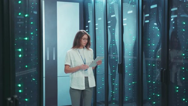 Smart female server engineer working with digital tablet at data center. Successful smiling woman administrator inspecting rack server computers in cyber security.