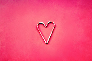 Christmas candy cane in a shape of heart, Valentine's day concept. Red background, flat lay.