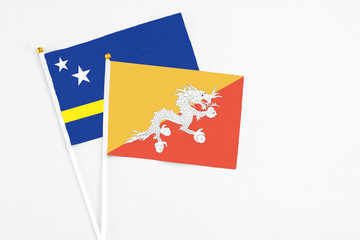 Bhutan and Curacao stick flags on white background. High quality fabric, miniature national flag. Peaceful global concept.White floor for copy space.
