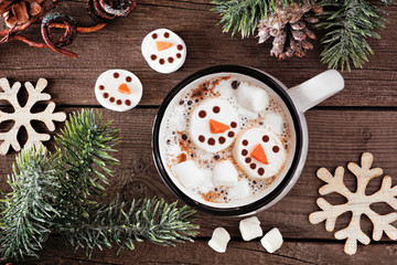 Hot chocolate with snowman marshmallows. Top view table scene with Christmas decor against a dark wood background.