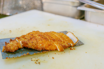 Pieces of sliced crispy chickens on cleaver knife and white plastic chopping block.