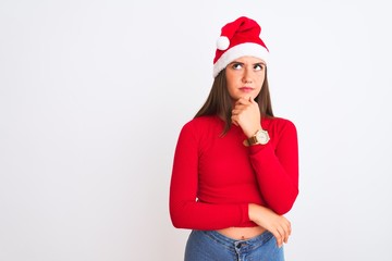 Young beautiful girl wearing Christmas Santa hat standing over isolated white background with hand on chin thinking about question, pensive expression. Smiling with thoughtful face. Doubt concept.
