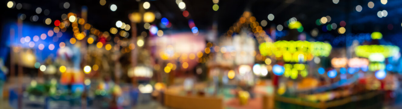 Beautiful blurry and defocused multicolored lights of the carousel in the night park. Panorama.