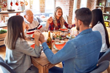 Beautiful family meeting smiling happy and confident. Praying taking hands before eating roasted turkey celebrating Christmas at home