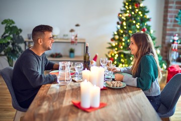 Young beautiful couple smiling happy and confident. Eating food celebrating christmas at home