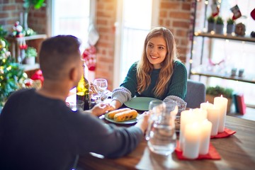 Young beautiful couple smiling happy and confident. Eating food celebrating christmas at home