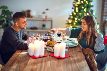 Young beautiful couple with dog smiling happy and confident. Eating food celebrating christmas at home
