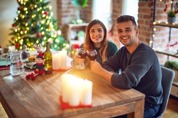 Young beautiful couple smiling happy and confident. Toasting with cup of wine celebrating christmas at home