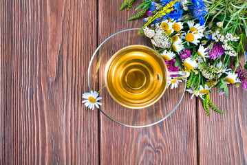 Herbal tea in a glass cup with bouquet of wild flowers on a wooden background. Text space. Top view.