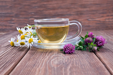 Green herbal tea with chamomile and pink clover flowers on a wooden background.