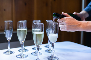 Crystal glasses that are standing on a white buffet table are being filled with an alcoholic beverage by the waiter