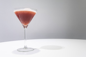 Cocktail glass with red colored cocktail in it on white table,  gray background. Drink concept. Sangria cocktail. Selective focus. Copy space. Horizontal.