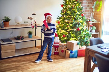 Obraz na płótnie Canvas Adorable toddler smiling happy and confident. Standing wearing santa claus hat with smile on face holding gift around christmas tree at home
