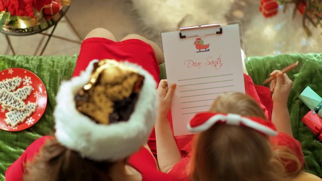 Upper view of elegant mother and daughter sitting on divan in the modern living room at Christmas writing letter to Santa Claus. This video was shot in PRORes 422 codec.
