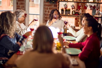 Beautiful group of women smiling happy and confident. Eating roasted turkey and toasting with cup of wine celebrating christmas at home