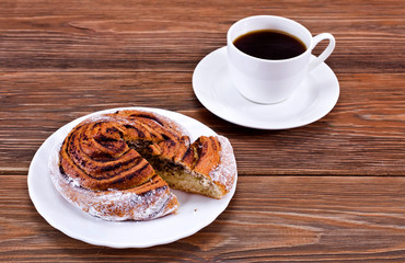 Cup of coffee and cinnamon bun on a wooden table.