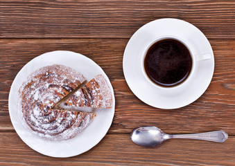 Cup of coffee and cinnamon roll (also cinnamon bun, cinnamon swirl, cinnamon snail) on a wooden table. Top view.
