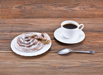 Cup of coffee and cinnamon roll (also cinnamon bun, cinnamon swirl, cinnamon snail) on a wooden table.