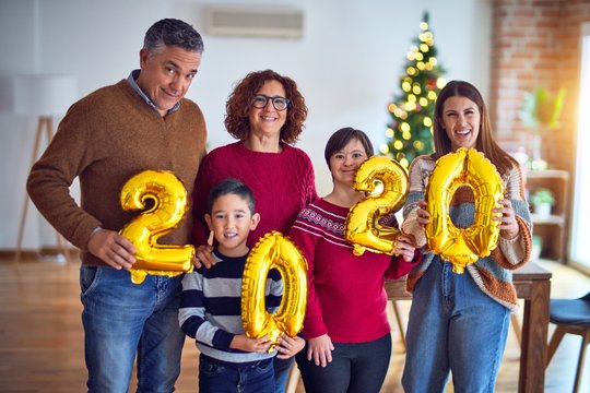 Beautiful family smiling happy and confident. Standing and posing holding 2020 balloons celebrating new year around christmas tree at home