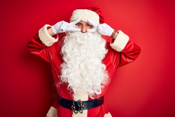 Middle age handsome man wearing Santa costume standing over isolated red background Doing peace symbol with fingers over face, smiling cheerful showing victory