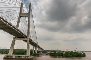 Ho Chi Minh City, Vietnam - March 12, 2019: Song Sai Gon river. One H-shaped pylon of Phu My suspension bridge and east side on ramp under gray cloudscape. Brown water. Long Tau river on right.
