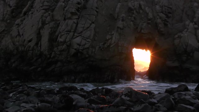 Zoom in shot of this magical rock at Pfeiffer Beach located in the Big Sur coastal area of Western California. The Pacific Ocean sunset lights up the keyhole rock as the sea waves rush through.   