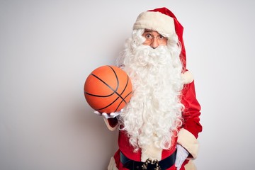 Senior man wearing Santa Claus costume holding basketball ball over isolated white background scared in shock with a surprise face, afraid and excited with fear expression