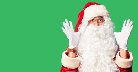 Middle age handsome man wearing Santa Claus costume and beard standing celebrating crazy and amazed for success with arms raised and open eyes screaming excited. Winner concept