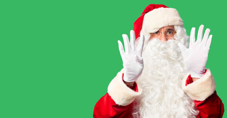 Middle age handsome man wearing Santa Claus costume and beard standing showing and pointing up with fingers number nine while smiling confident and happy.