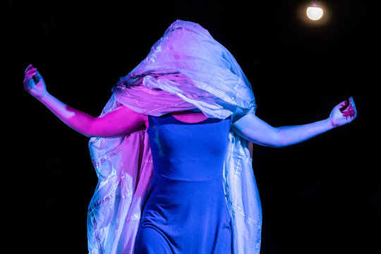 Adult woman with large cloth covering her head and shoulders performing a drama play on stage in a theatrical show 