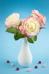 Light roses close up in a white vase on a blue background. Holiday card with pink roses on Valentine's Day or March 8 with copy space.