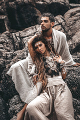beautiful young wild free couple in tribal costumes at the stone background