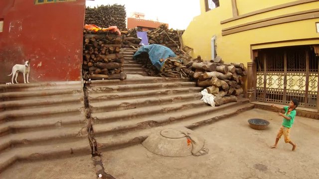 little indian boy plays with kite throwing and crashes it beton aria with stairs and piles of firewoods Manikarnika Ghat
