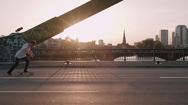 skateboarder pushing on bridge in super slow motion in front frankfurt skyline skyscrapers sunset
