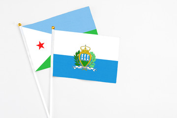 San Marino and Djibouti stick flags on white background. High quality fabric, miniature national flag. Peaceful global concept.White floor for copy space.